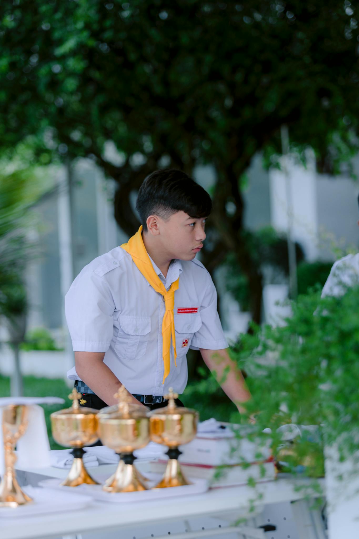 Scout boy in uniform organizing a table with gold cups outdoors.